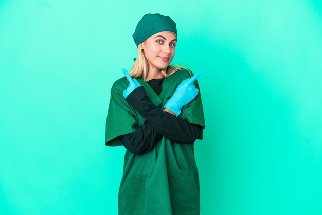 Joven cirujana uruguaya con uniforme verde aislada de fondo azul apuntando a los laterales con dudas