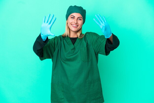 Joven cirujana uruguaya con uniforme verde aislada de fondo azul contando nueve con los dedos