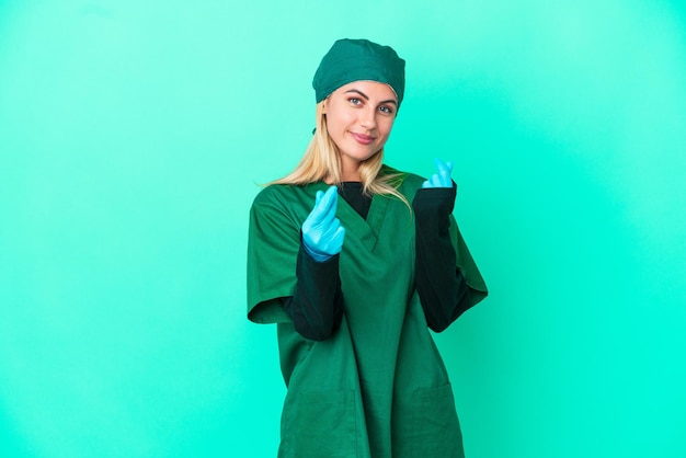 Joven cirujana uruguaya con uniforme verde aislada de fondo azul haciendo gestos de dinero