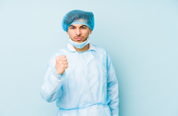 Joven cirujano árabe hombre contra una pared azul que muestra el puño a la cámara