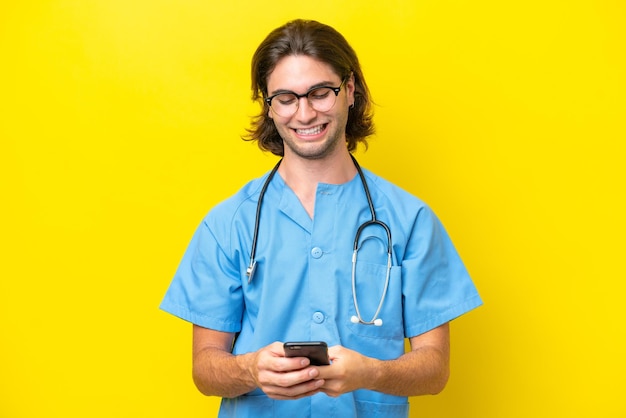 Joven cirujano caucásico aislado de fondo amarillo enviando un mensaje con el móvil