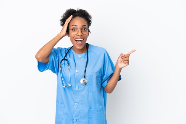 Joven cirujano médico afroamericano mujer aislada sobre fondo blanco sorprendido y apuntando con el dedo hacia el lado