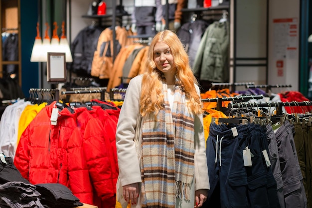 Una joven clienta con cabello dorado eligiendo ropa en una tienda de ropa moderna