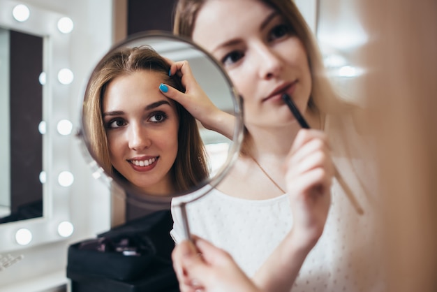 Joven clienta mirando en el espejo mientras la maquilladora trabajaba en sus cejas en el salón de belleza