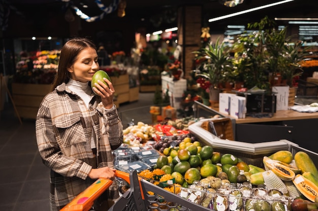 Una joven clienta de un supermercado huele un fragante mango maduro