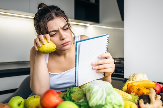 Foto una joven en la cocina con un cuaderno entre verduras.