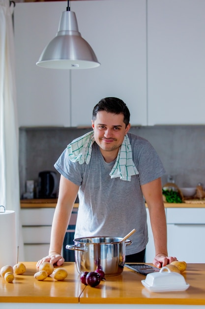 Joven cocinando en la cocina por sí mismo con patatas y cebolla.