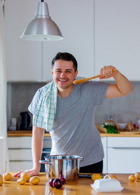 Joven cocinando en la cocina por sí mismo con patatas y cebolla.