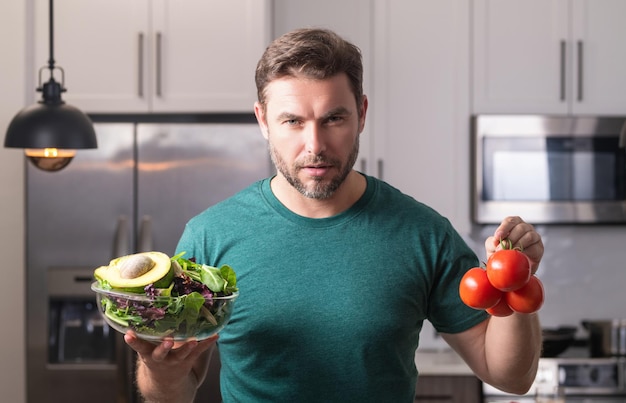 Joven cocinando ensalada vegana saludable en la cocina hombre milenario en la mesa de la cocina moderna chop vegetab