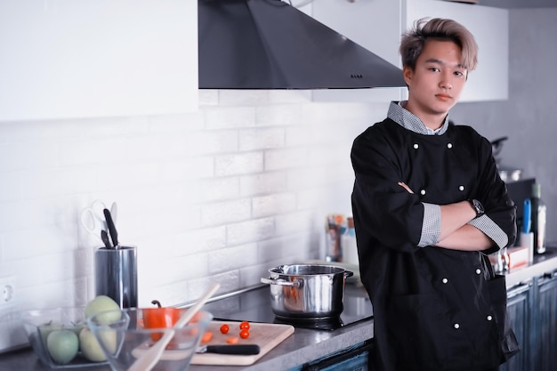 Un joven cocinero asiático en la cocina prepara la comida con un traje de cocinero