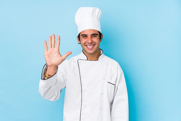 Joven cocinero hombre aislado sonriente alegre mostrando número cinco con los dedos.