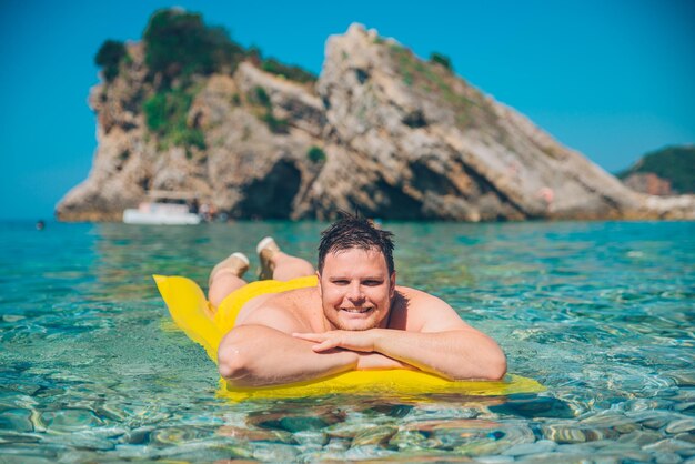 Joven en colchón inflable amarillo en agua clara y transparente