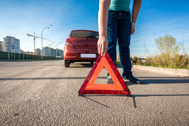 Joven colocando triángulo rojo canta en la carretera después de un accidente de coche