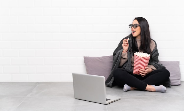 Joven colombiana en una habitación con gafas 3d y sosteniendo un gran cubo de palomitas de maíz