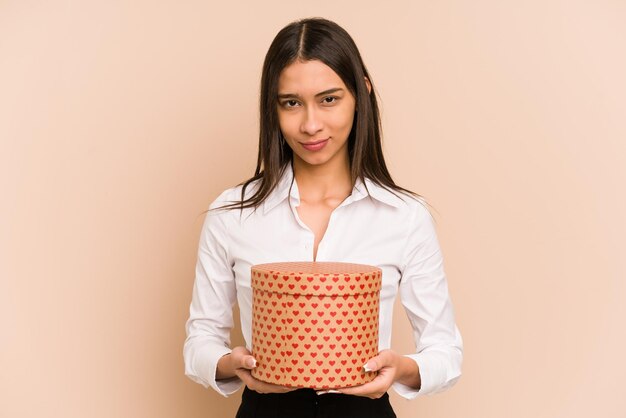 Joven colombiana sosteniendo un regalo del día de san valentín aislado sobre fondo beige