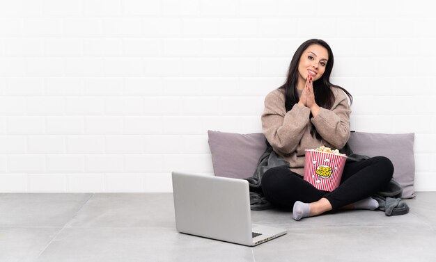 Joven colombiana sosteniendo un tazón de palomitas de maíz y mostrando una película en una computadora portátil aplaudiendo después de la presentación en una conferencia