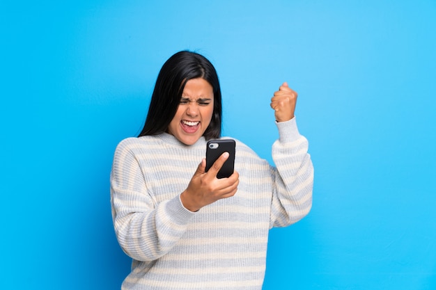 Joven colombiana con suéter celebrando una victoria con un móvil