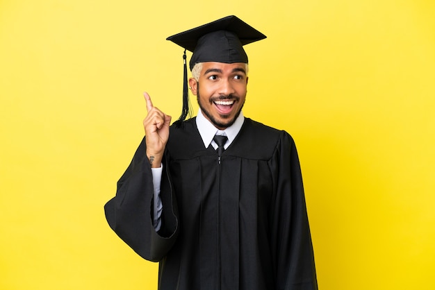 Joven colombiano graduado universitario aislado sobre fondo amarillo con la intención de darse cuenta de la solución mientras levanta un dedo hacia arriba