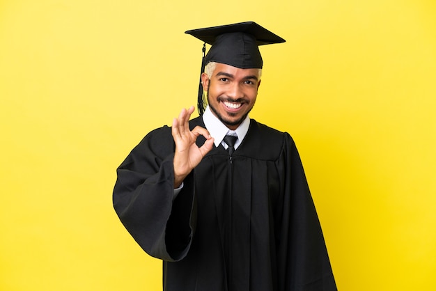 Joven colombiano graduado universitario aislado sobre fondo amarillo mostrando el signo de ok con los dedos