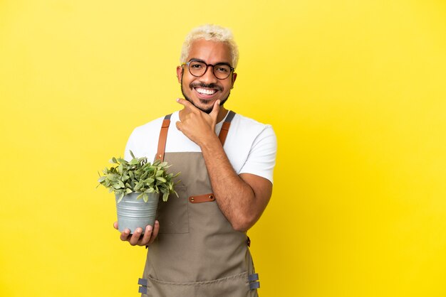 Joven colombiano sosteniendo una planta aislada sobre fondo amarillo feliz y sonriente