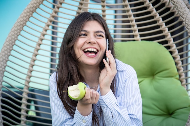 Una joven come una manzana con un teléfono inteligente en las manos.