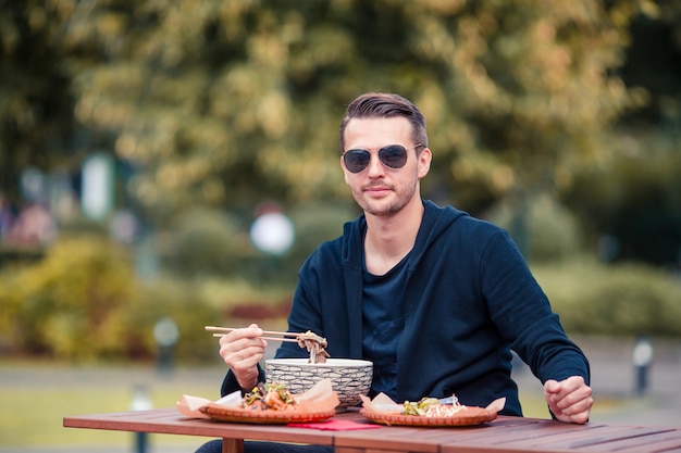 Joven comiendo para llevar fideos en la calle