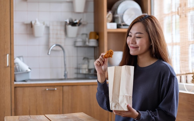 Una joven comiendo pollo frito de una bolsa de papel en la cocina de su casa para el concepto de entrega de alimentos