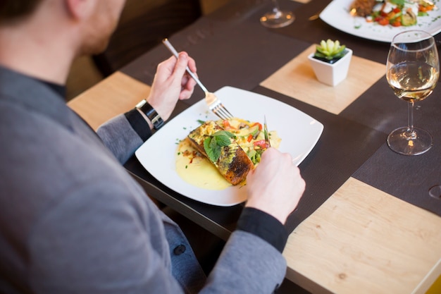 Joven comiendo salmón a la plancha con salsa y hierbas servido en el restaurante