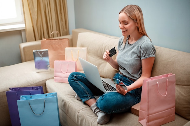 Joven comprador feliz con tarjetas de crédito sentado en un sofá con bolsas de compras