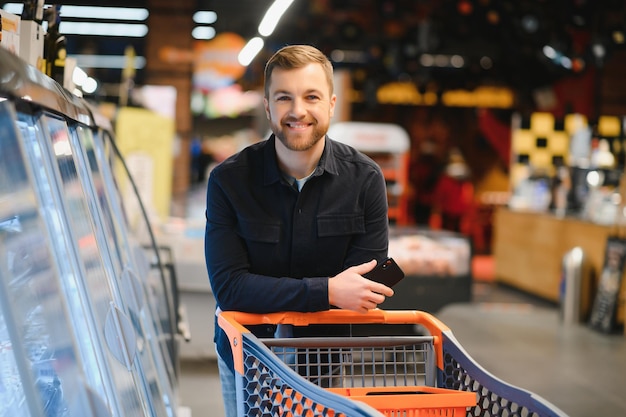 Joven comprando comestibles en el supermercado Otros clientes en segundo plano Concepto de consumismo