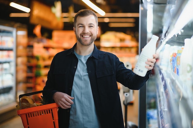 Joven comprando comestibles en el supermercado Otros clientes en segundo plano Concepto de consumismo