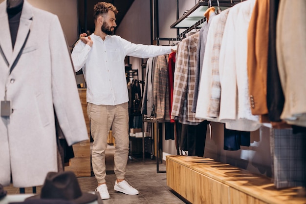 Joven comprando en la tienda de ropa masculina y hablando por teléfono | Foto