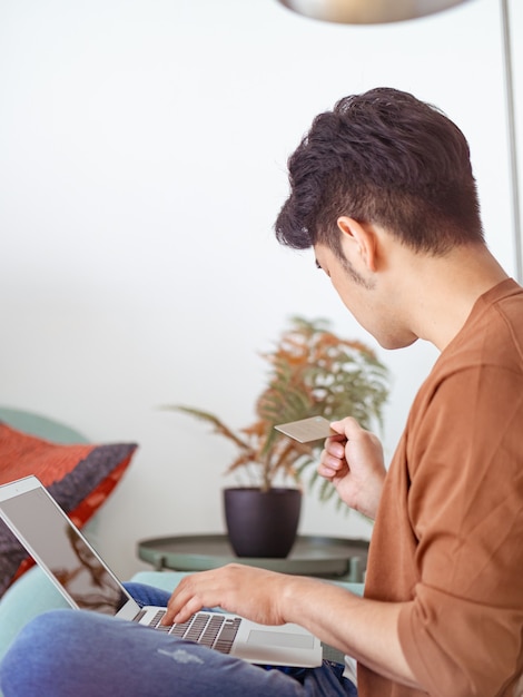 Joven de compras online con tarjeta de crédito y portátil en casa