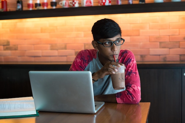 Un joven con una computadora portátil bebiendo café mientras está sentado en una cafetería