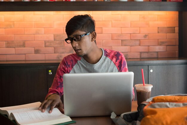 Joven con computadora portátil estudiando en una cafetería