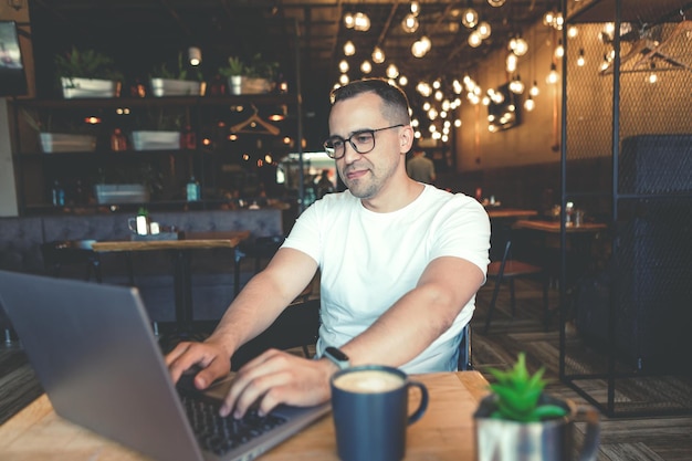 Un joven con una computadora portátil se sienta en un café.