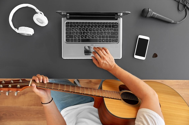 un joven con una computadora portátil tocando la guitarra en la mesa