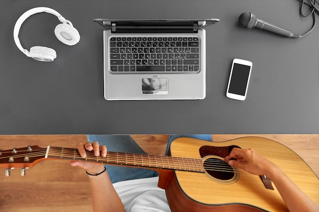 un joven con una computadora portátil tocando la guitarra en la mesa