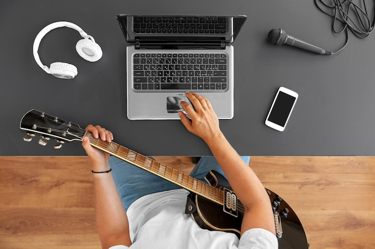 Foto un joven con una computadora portátil tocando la guitarra en la mesa