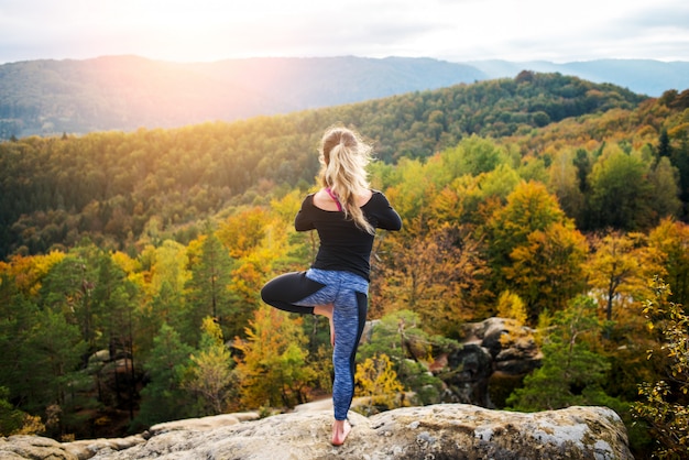 Joven concentrada está practicando yoga en la cima de la montaña en la noche