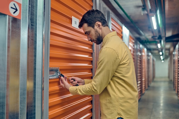 Joven concentrado cerrando con candado la puerta de la unidad de almacenamiento