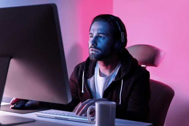 Un joven concentrado mirando el monitor de la computadora mientras está sentado contra un fondo colorido