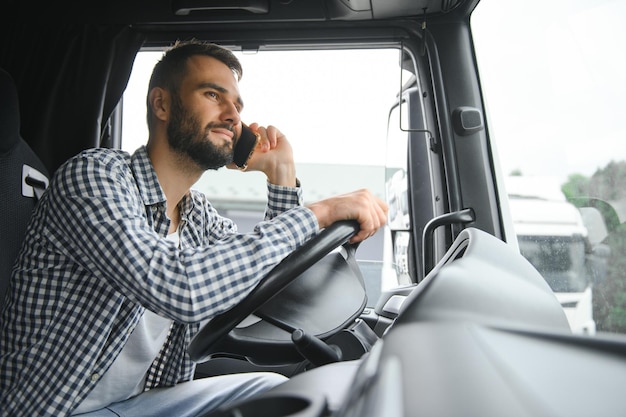 Joven conductor profesional comunicándose por teléfono móvil mientras conduce un camión