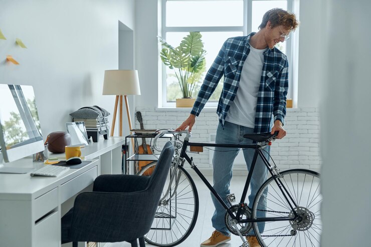 Un joven confiado examinando su bicicleta mientras está de pie cerca de su lugar de trabajo en casa