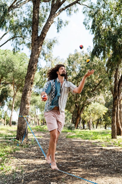 Joven confiado haciendo malabares y balanceándose en el slackline en el parque de la ciudad