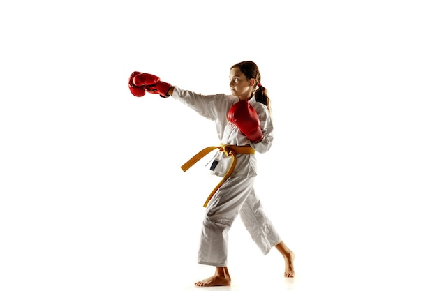 Joven confiado en kimono practicando combate cuerpo a cuerpo, artes marciales. Joven luchadora con entrenamiento de cinturón amarillo en la pared blanca. Concepto de estilo de vida saludable, deporte, acción.