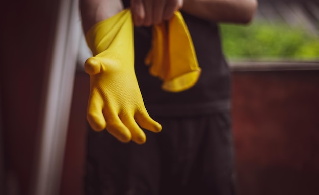 Un joven constructor caucásico irreconocible con uniforme negro se pone guantes de goma amarillos vista desde abajo El concepto de trabajos de construcción de renovación de viviendas