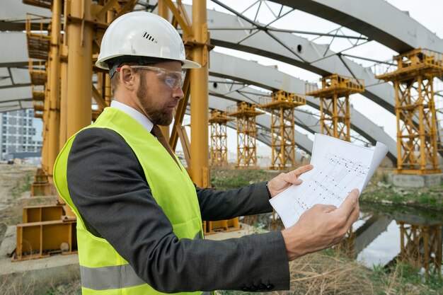 Joven constructor serio mirando boceto en papel mientras trabaja