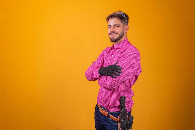 Joven contratista o electricista sobre fondo amarillo con los brazos cruzados.