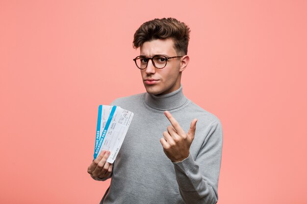 Joven cool con un billete de avión apuntando con el dedo hacia ti como invitando a acercarse.